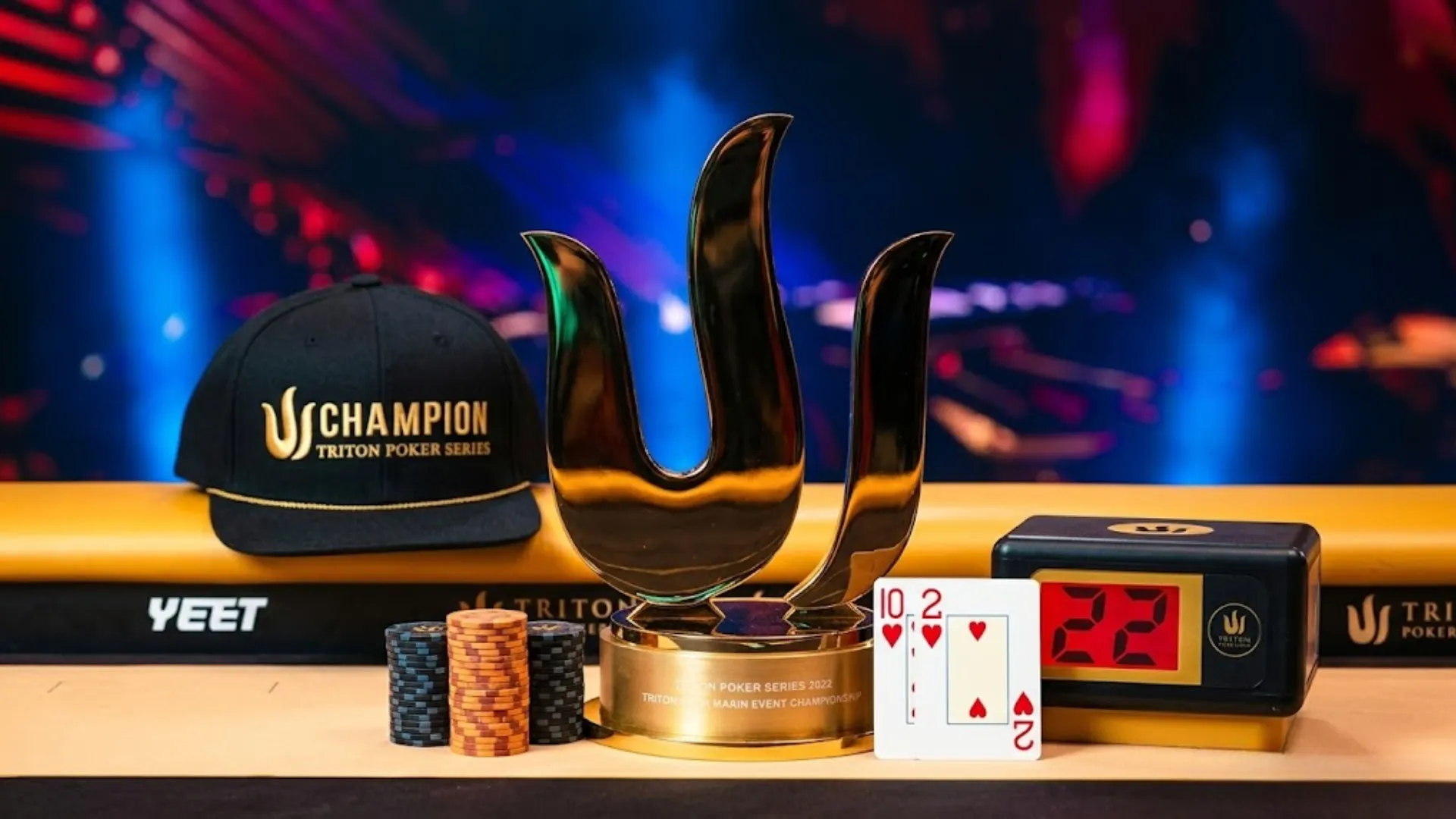 Triton Poker Series champion trophy with 10-2 of hearts winning hand cards, poker chips, and Champion cap on the final table — Ben Tollerene wins Triton Jeju Main Event 2026